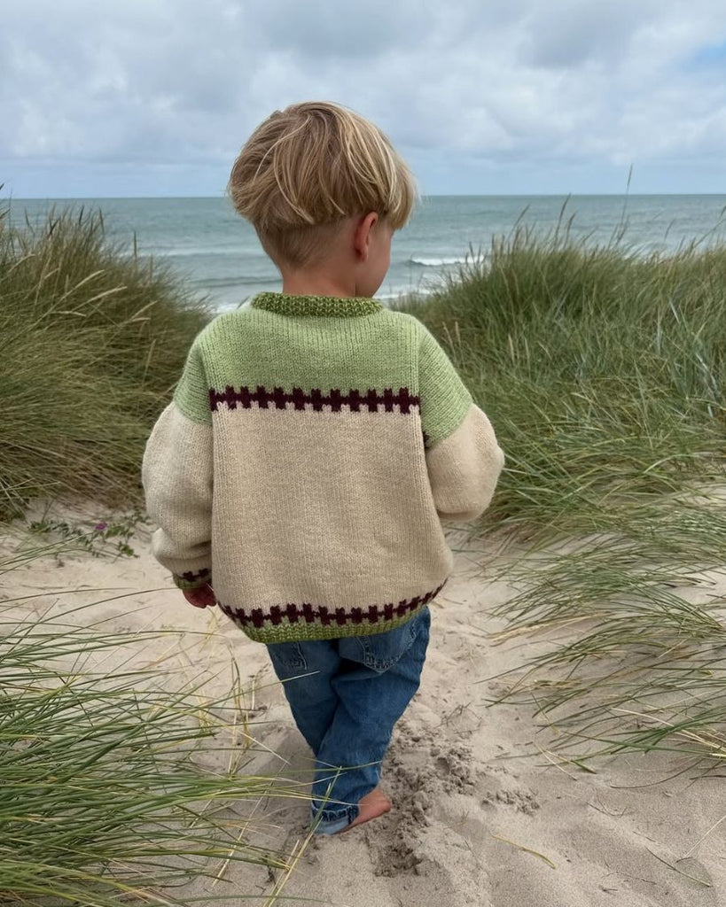 Barn set bagfra iført grøn og hvid Cross Sweater Junior