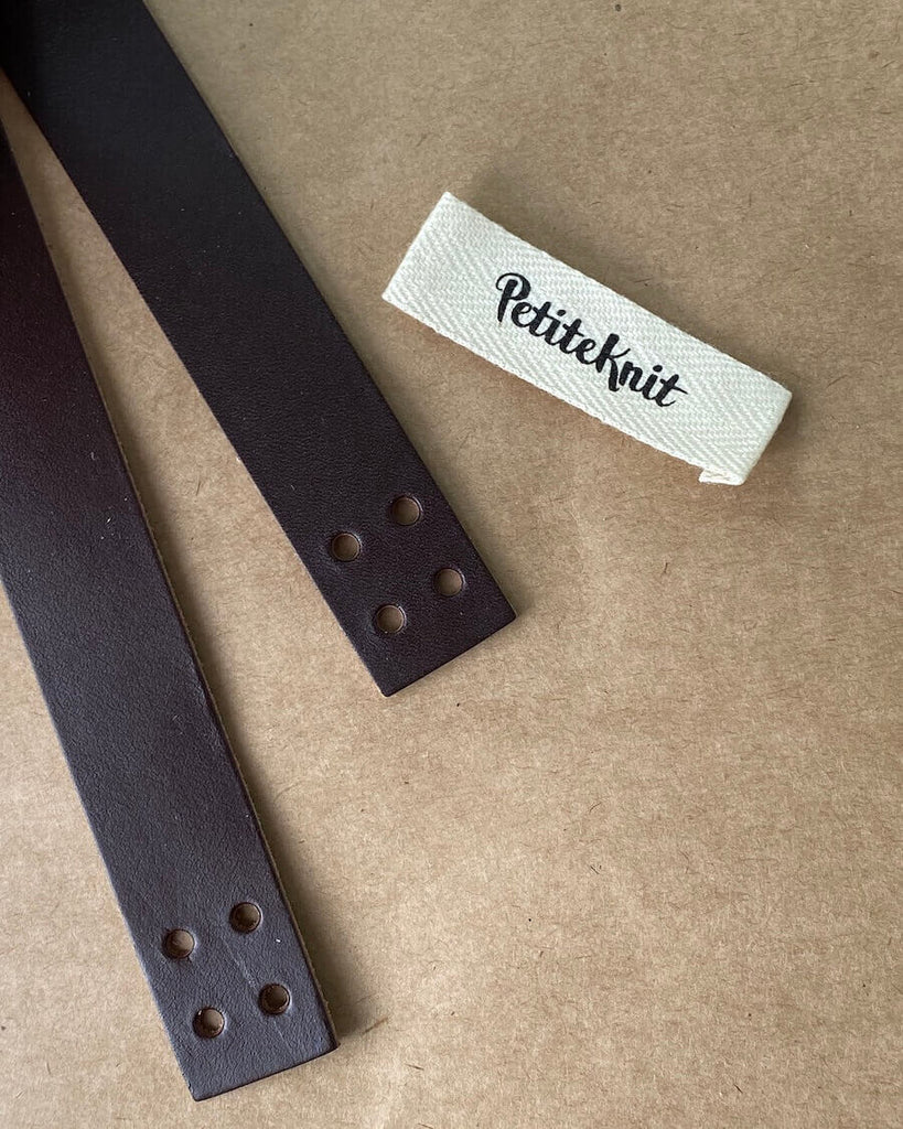 Detaljer af mæørk læderstrop med huller og Petiteknit label