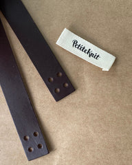 Detaljer af mæørk læderstrop med huller og Petiteknit label