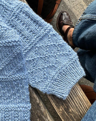 Detaljebillede af lyseblå Storm Sweater Baby liggende på bænk