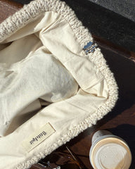 Åbentstående beige Teddy Clutch på bænk