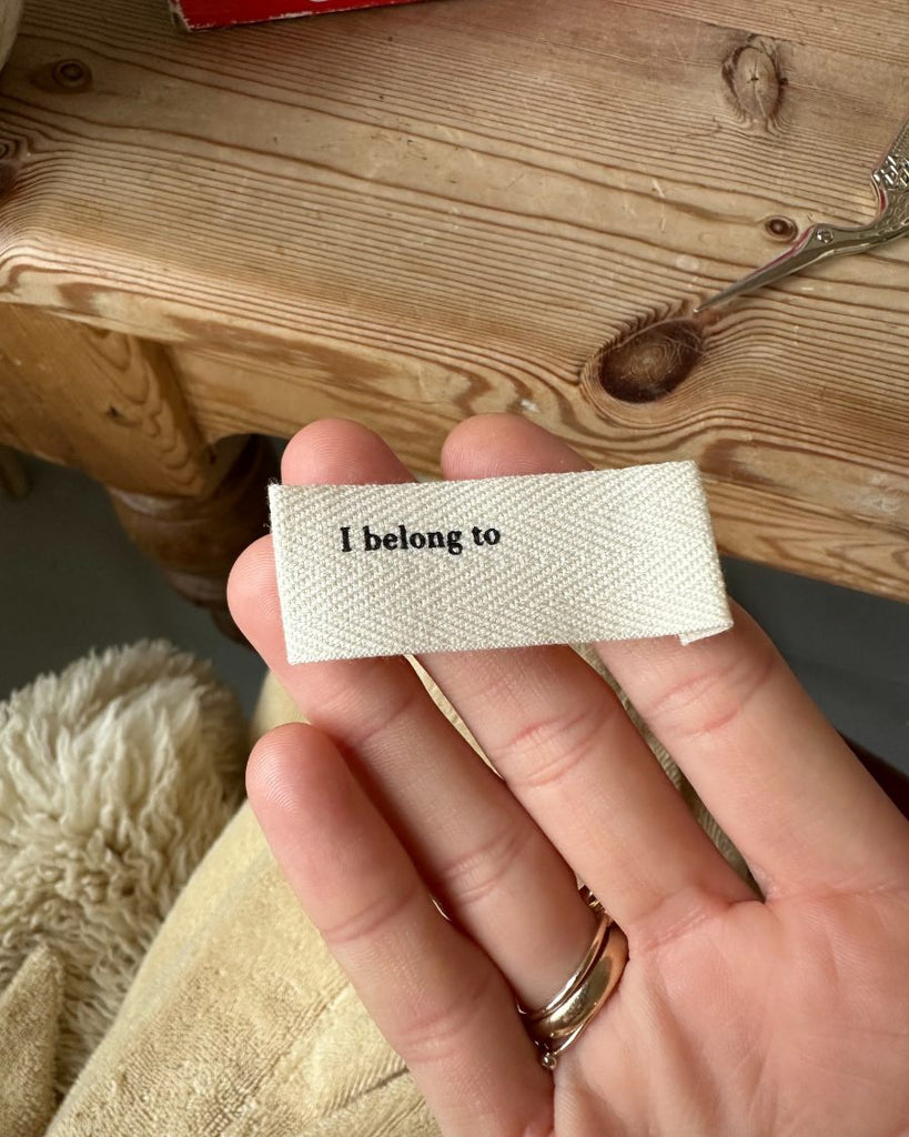 Label med "i belong to" på hånd