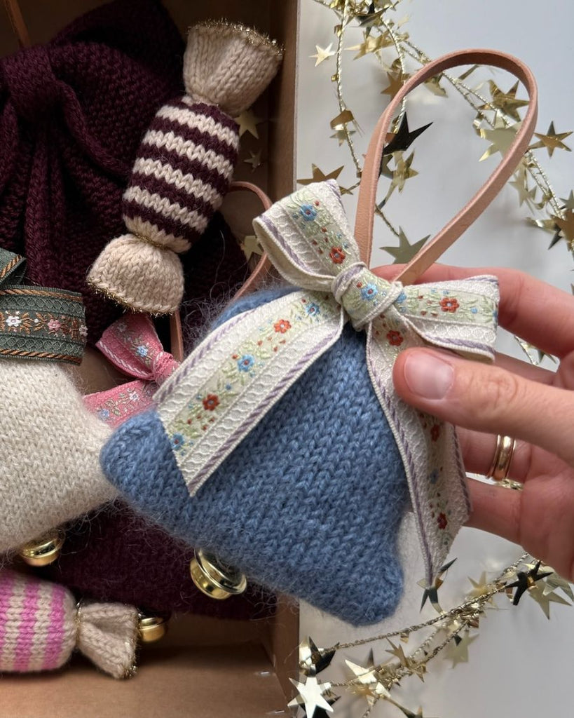 Hånd holder blå Christmas Bell over kasse med andet strikke julepynt