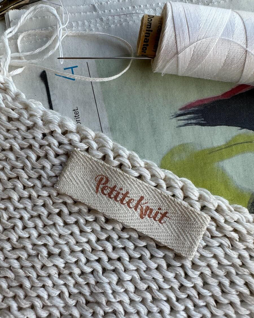Label med Petiteknit logo i biscuit farve på strik