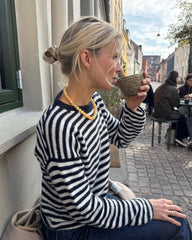 Kvinde iført hvid og blå Olga Blouse siddende på bænk med kaffe