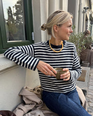 Kvinde iført hvid og blå Olga Blouse siddende på bænk med kaffe