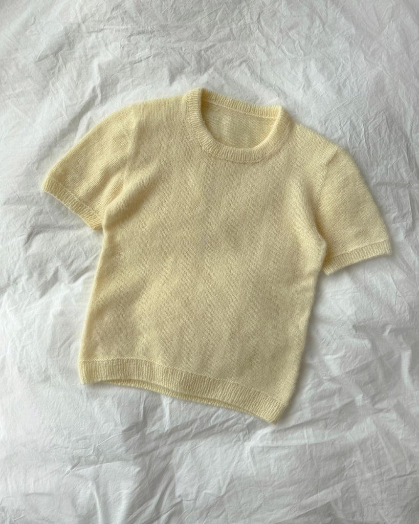 Gul oppy Tee liggende på sengetøj